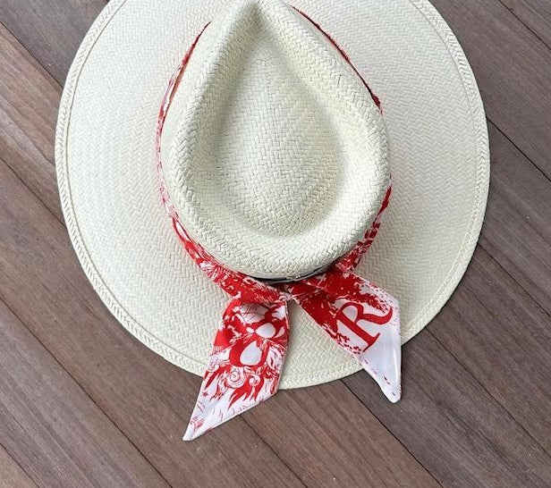 White straw hat with a red and white patterned bandana on a wooden surface